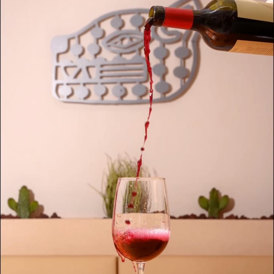 Red wine pouring from a bottle into a glass, with decorative cacti and a wall art in the background.