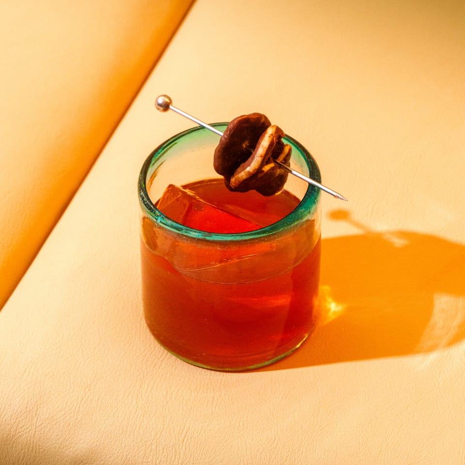 A Balam Coffee & Wine cocktail with ice and a chocolate-covered orange garnish on a light orange surface.